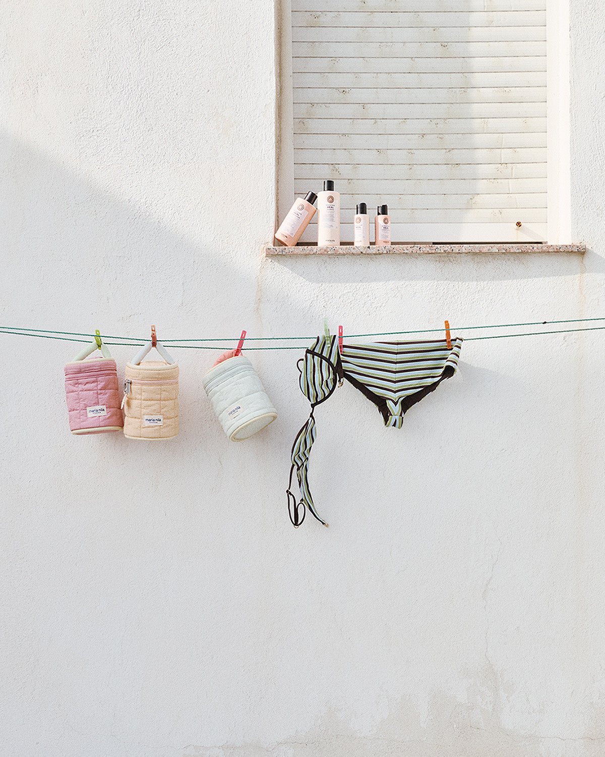 Bathing suits and Beauty Bags hanging on a clothesline against a white wall.