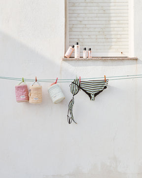 Bathing suits and Beauty Bags hanging on a clothesline against a white wall.