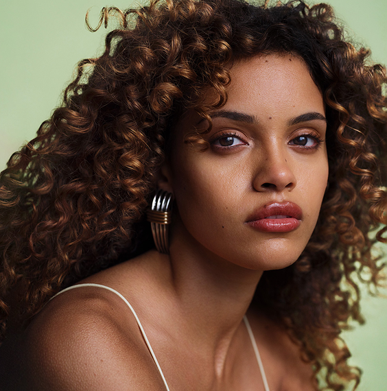 Model with curly brown hair against light green background