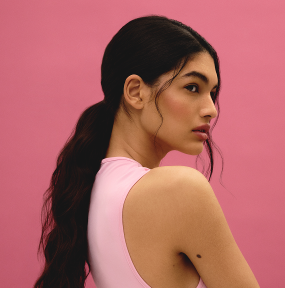 Model with dark hair in low ponytail against pink background