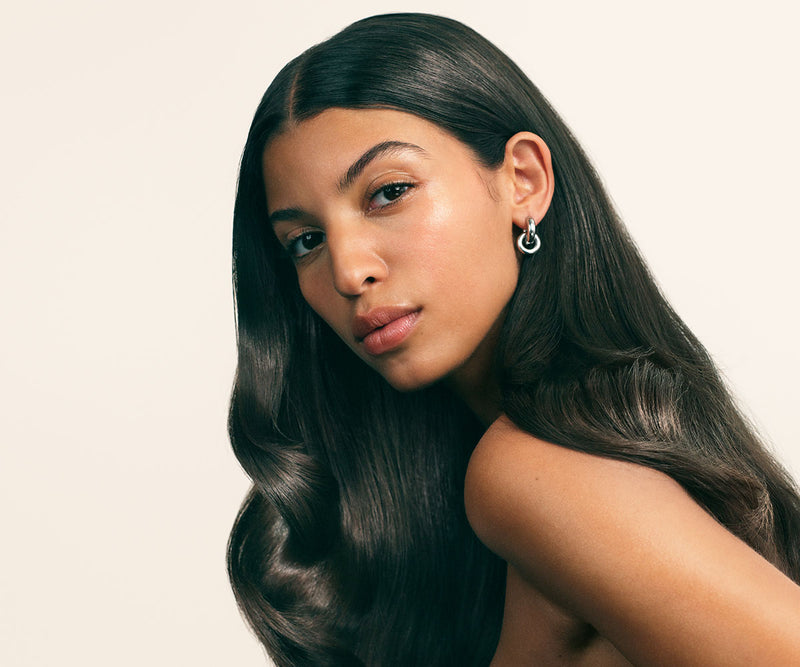 Woman with dark, shiny wavy hair against a beige backdrop