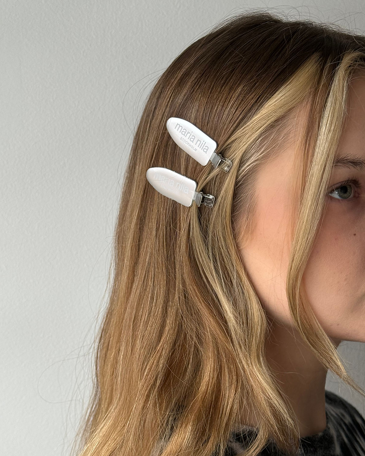 Person wearing a white hair clip with 'Maria Nila' branding on a plain background