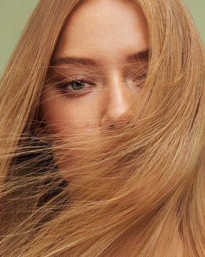 Close-up of a person with long blonde hair in Color Refresh Beige Blonde covering part of their face against a light green background